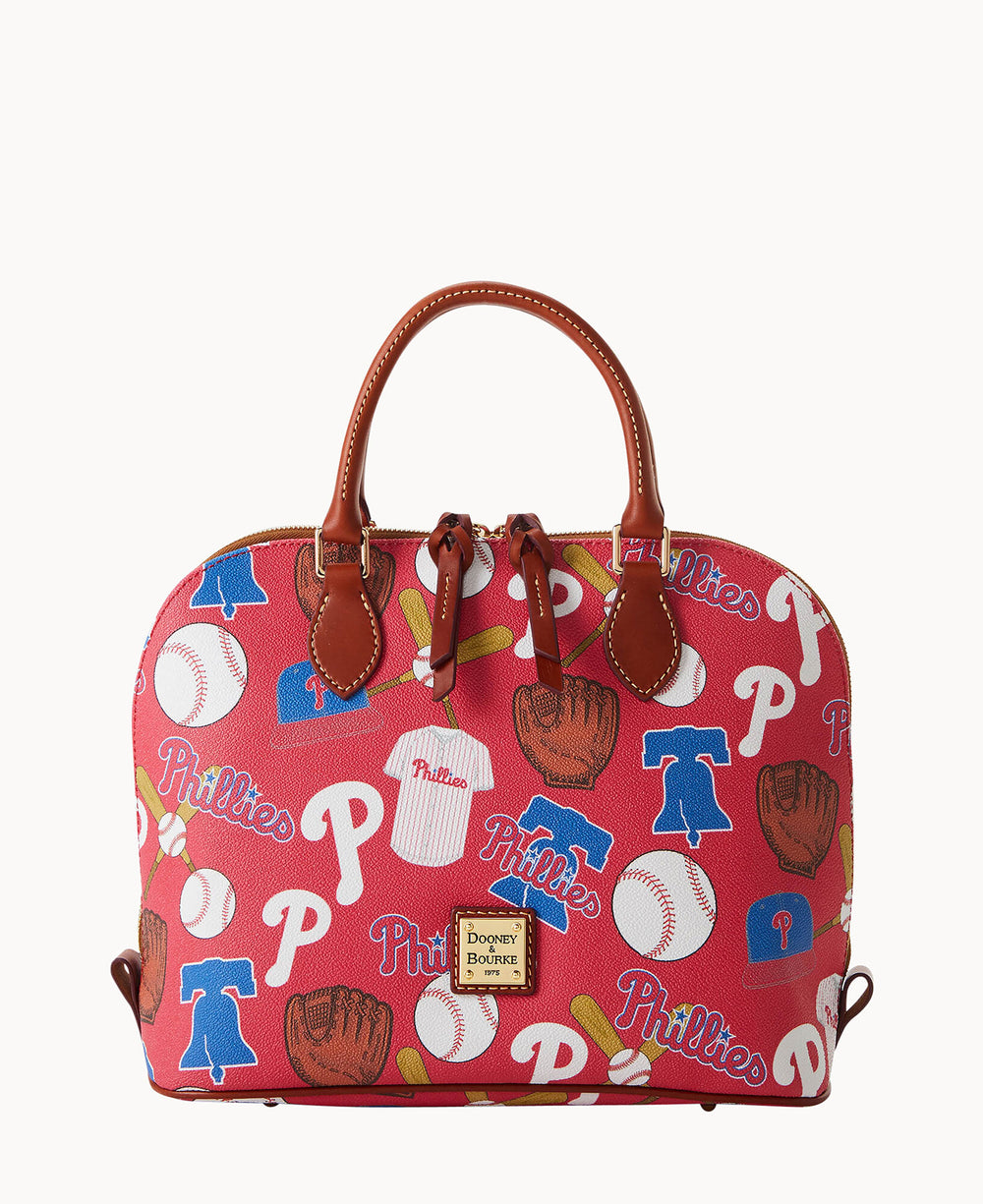 A red Dooney & Bourke handbag featuring a Philadelphia Phillies baseball-themed print with baseballs, gloves, jerseys, and team logos. The bag has brown leather handles and trim.