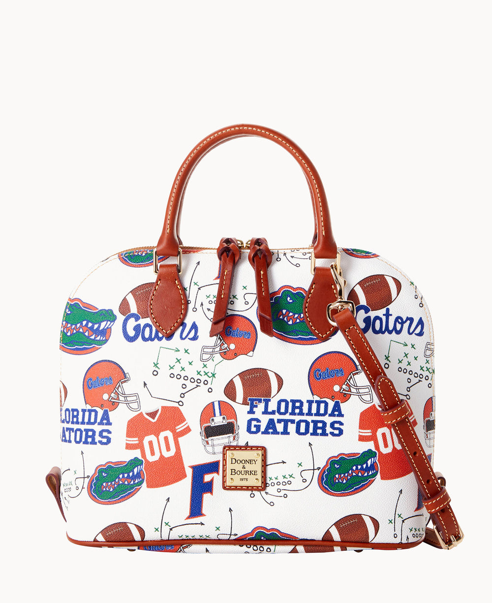 A white Dooney & Bourke handbag with brown leather handles, decorated with Florida Gators logos, footballs, jerseys, helmets, and play diagrams in orange, blue, and green.
