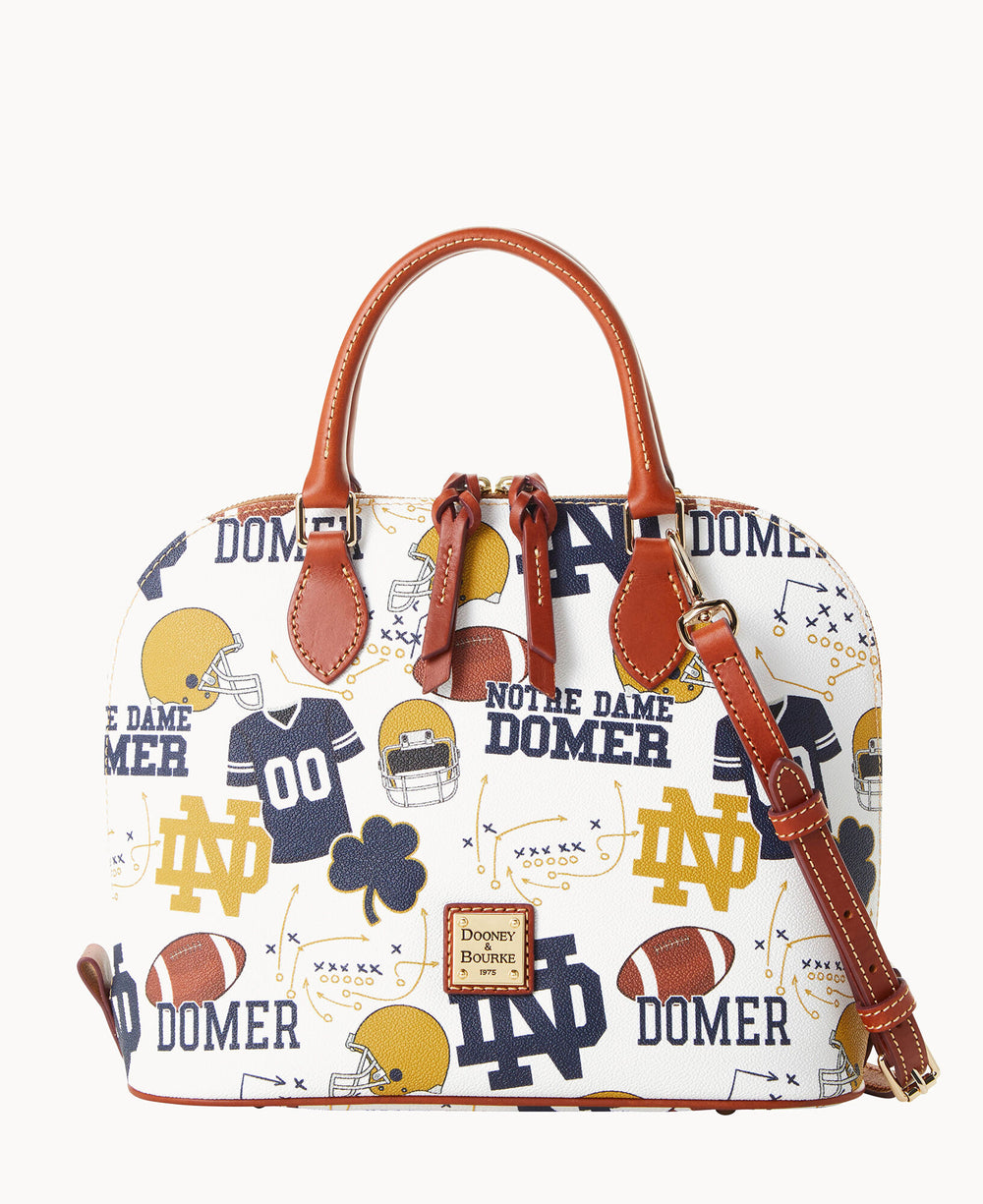 A white Dooney & Bourke handbag featuring Notre Dame-themed graphics, including football helmets, jerseys, shamrocks, footballs, and ND logos, with brown leather handles and trim.