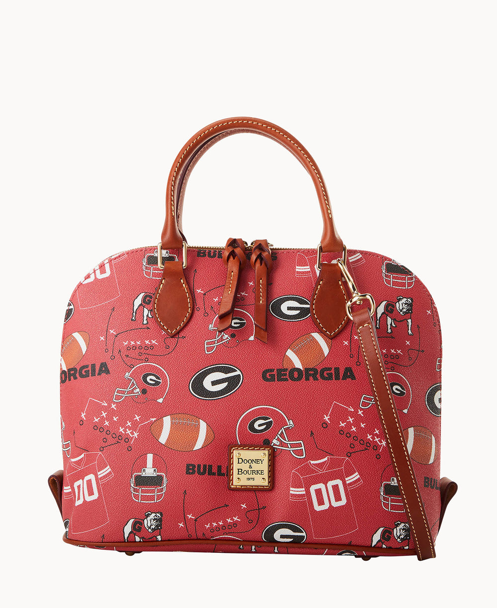 A red Dooney & Bourke handbag features brown leather handles and a strap, decorated with University of Georgia football-themed graphics, including helmets, footballs, jerseys, and the words Georgia and Bulldogs.