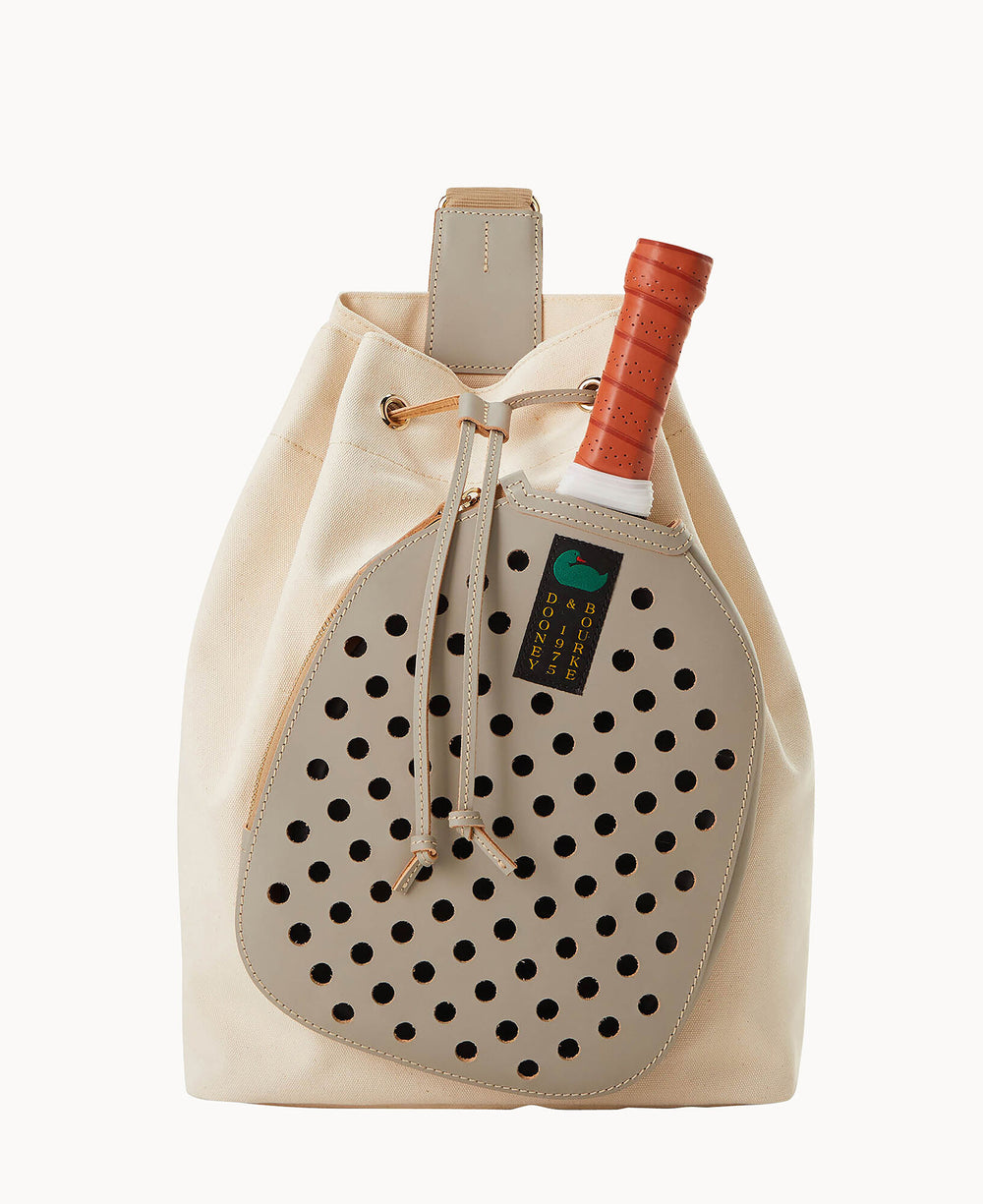 A beige canvas backpack with tan leather accents, featuring a perforated leather pocket holding a paddle and a paddle with an orange handle partially tucked inside.