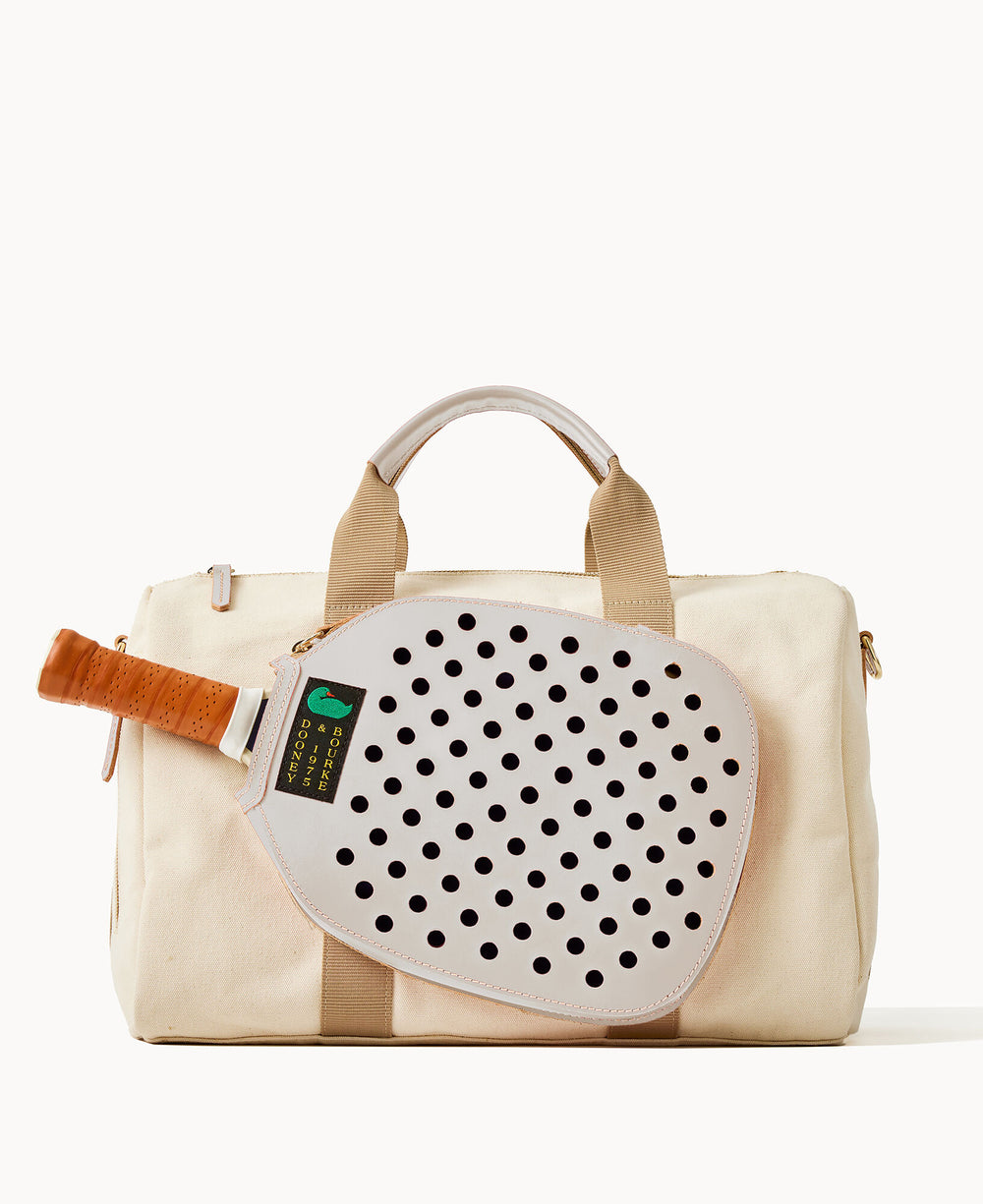 A cream-colored duffel bag with tan handles and trim, carrying a white perforated paddle with a tan grip attached to the front.