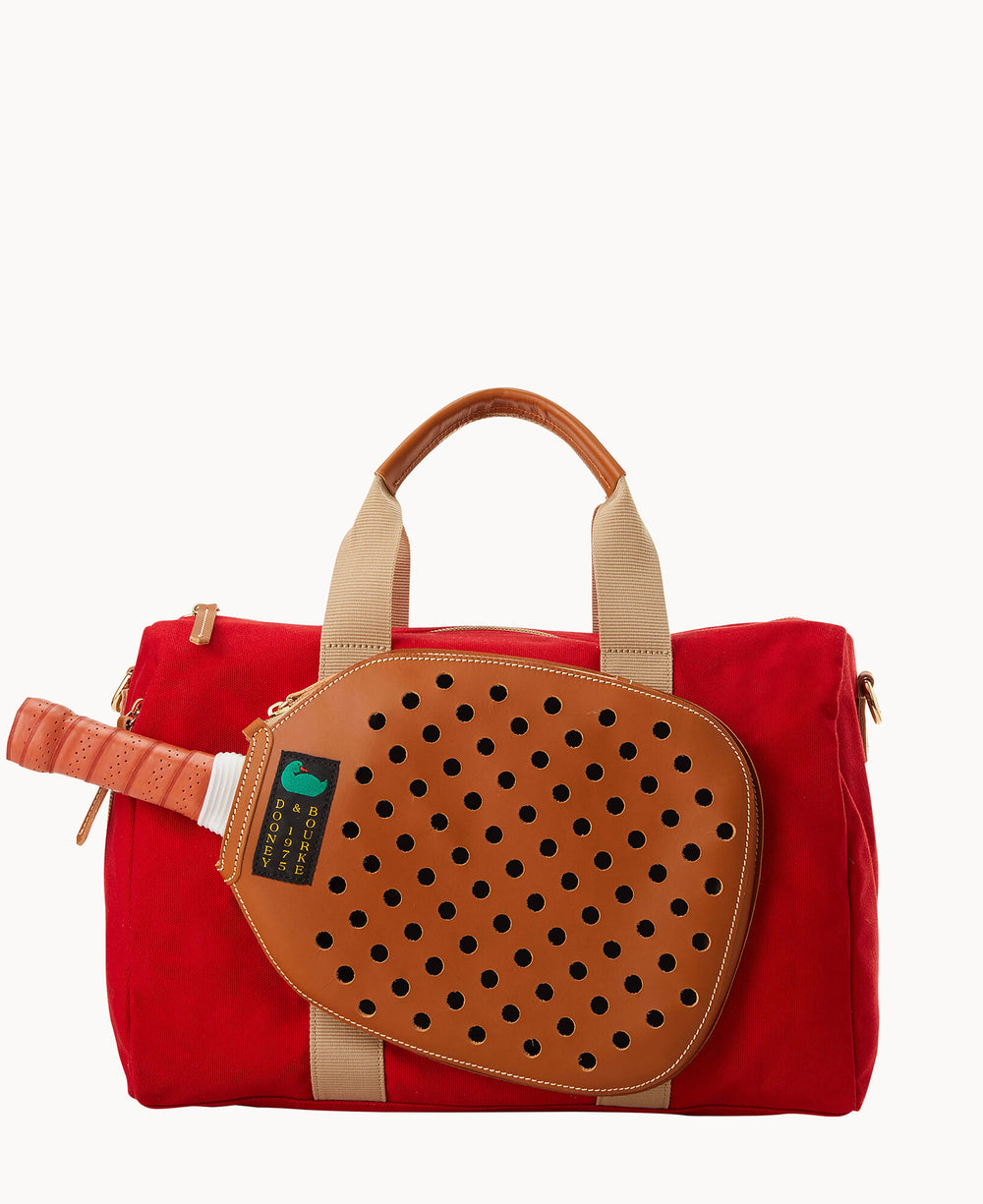 A red duffel bag with beige handles and accents, featuring a brown leather paddle cover with black ventilation holes attached to the front. A paddle with a wrapped handle is partially inserted in the cover.