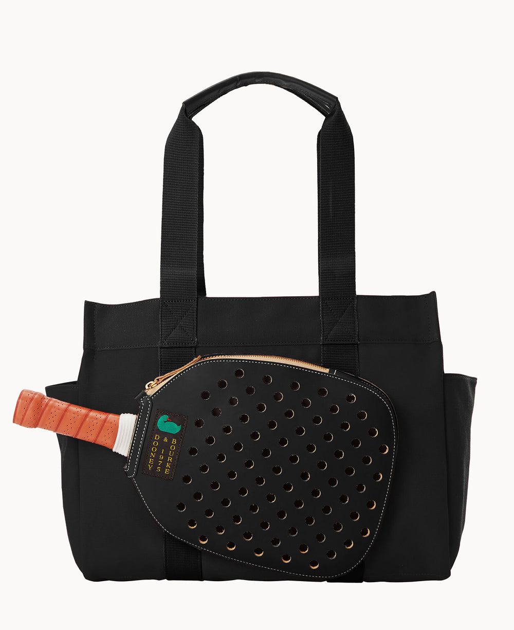 A black tote bag with wide handles and external side pockets, featuring a pickleball paddle with an orange handle partially zipped inside a front mesh pocket.