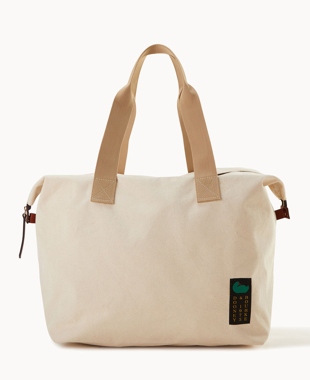 A large beige canvas tote bag with sturdy tan handles, a zipper closure, and a small green and black rectangular tag attached to one handle. The bag is displayed against a plain white background.