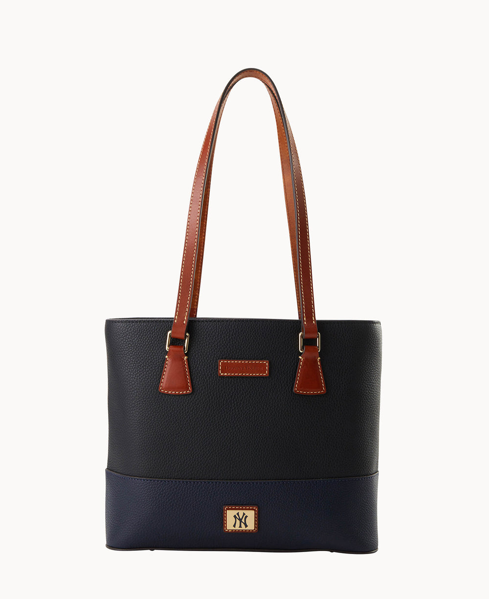 A navy blue leather tote bag with brown leather handles and trim, gold-tone hardware, and a small rectangular logo patch at the bottom center. The bag has a simple, structured design against a white background.