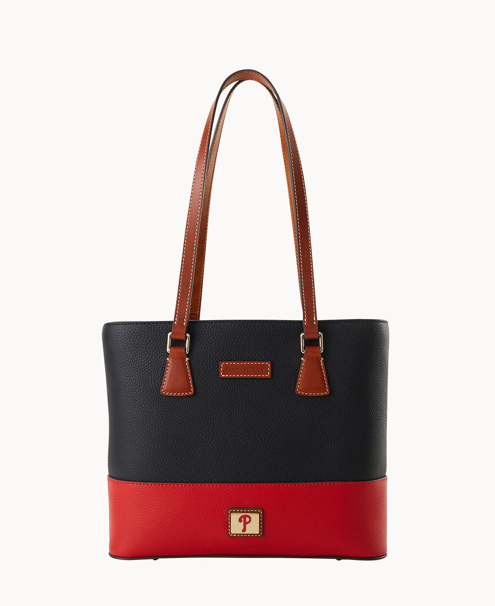A colorblock tote bag with brown handles, a navy blue upper section, and a red lower section. A small rectangular logo patch with a â€œPâ€ is on the red panel at the bottom front of the bag.