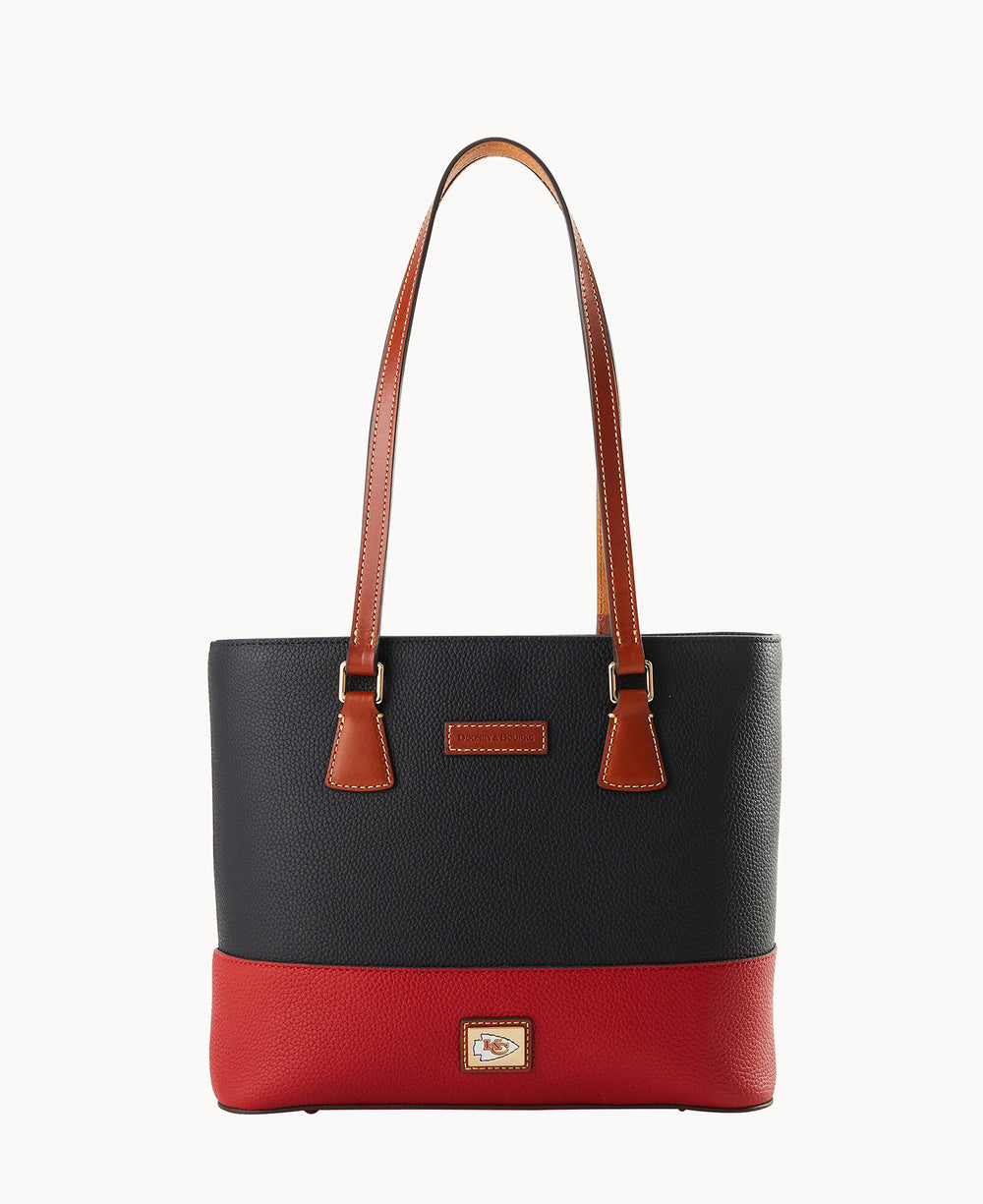 A stylish tote bag with long brown leather straps, a textured black upper section, and a red bottom section. There is a small rectangular logo patch at the center of the red portion.