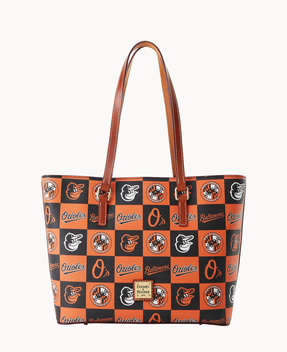 A tote bag with brown handles featuring a checkered pattern of the Baltimore Orioles logos and the word â€œOriolesâ€ in orange, black, and white. The bag has a Dooney & Bourke label on the front.