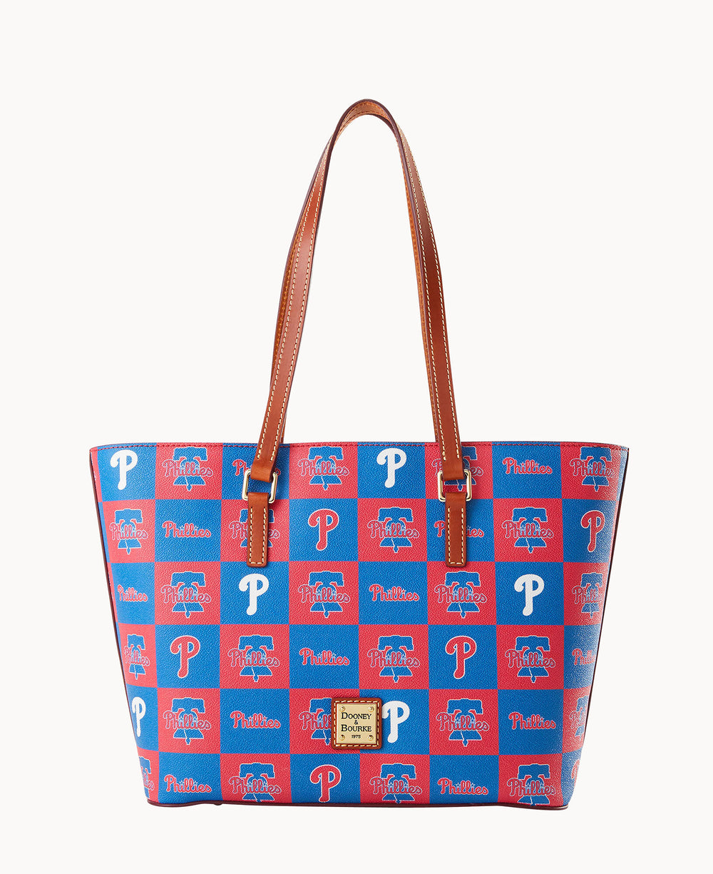 A tote bag with brown handles features a red and blue checkerboard pattern, decorated with Philadelphia Phillies logos and text. The front has a gold Dooney & Bourke label.