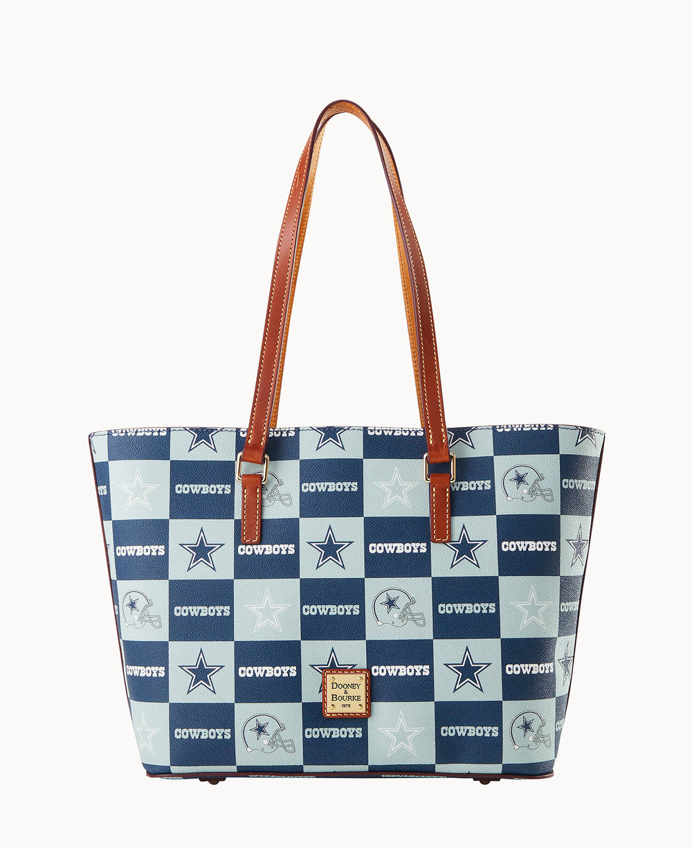 A tote bag with brown handles and a blue checkered pattern featuring the Dallas Cowboys logo, stars, and the word COWBOYS. A Dooney & Bourke label is on the front.