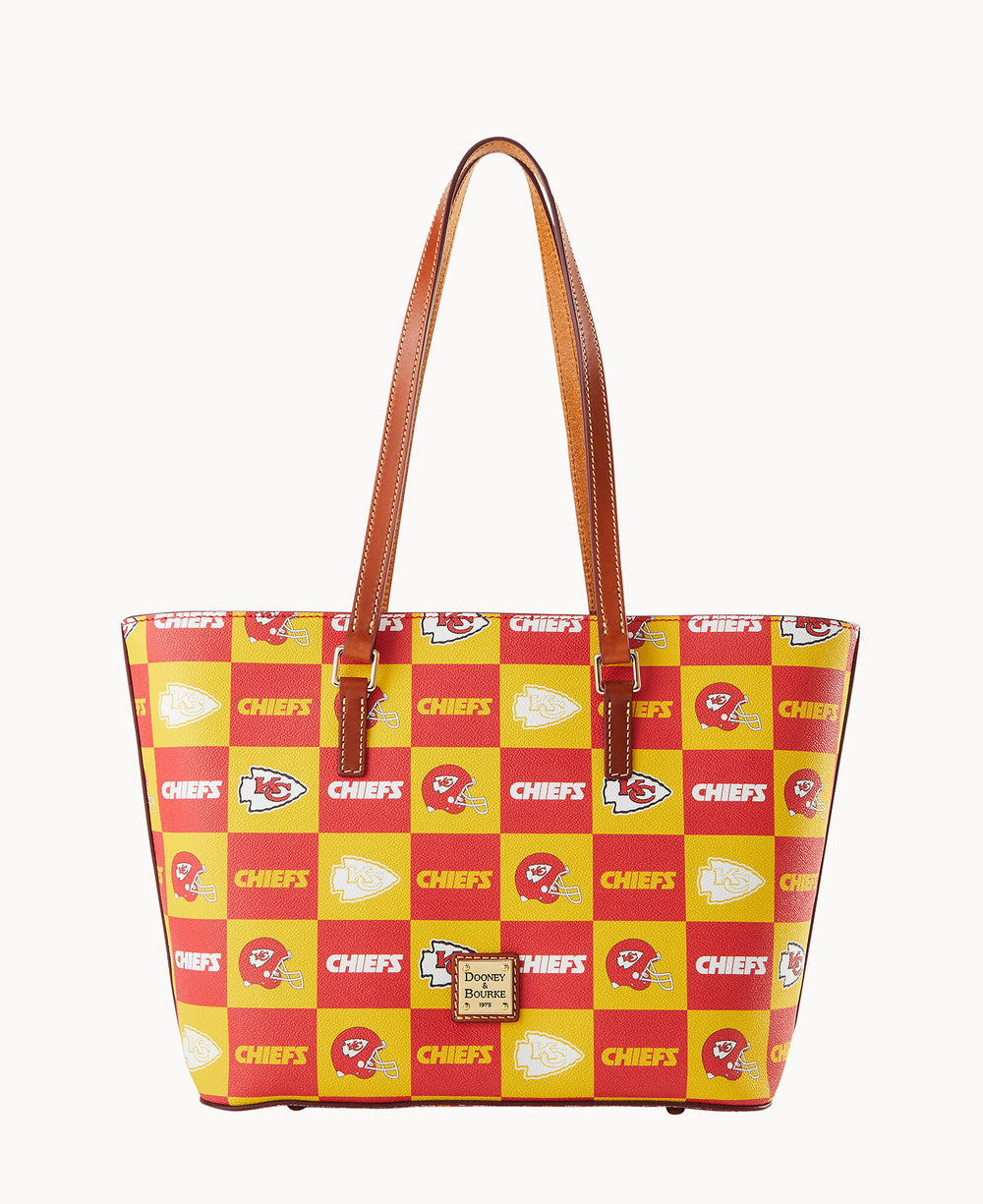 A tote bag with brown handles featuring a red and yellow checkerboard pattern with Kansas City Chiefs logos, football helmets, and the word CHIEFS printed on the squares.