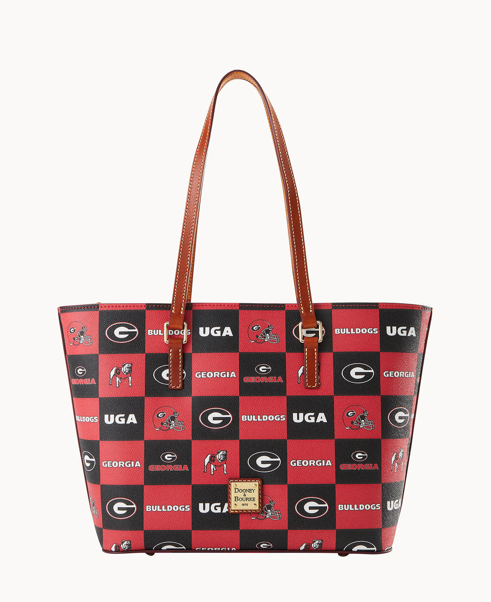 A red and black tote bag with brown handles, featuring a checkered pattern with University of Georgia logos, bulldogs, the word BULLDOGS, and UGA. The brand label Dooney & Bourke is on the front.