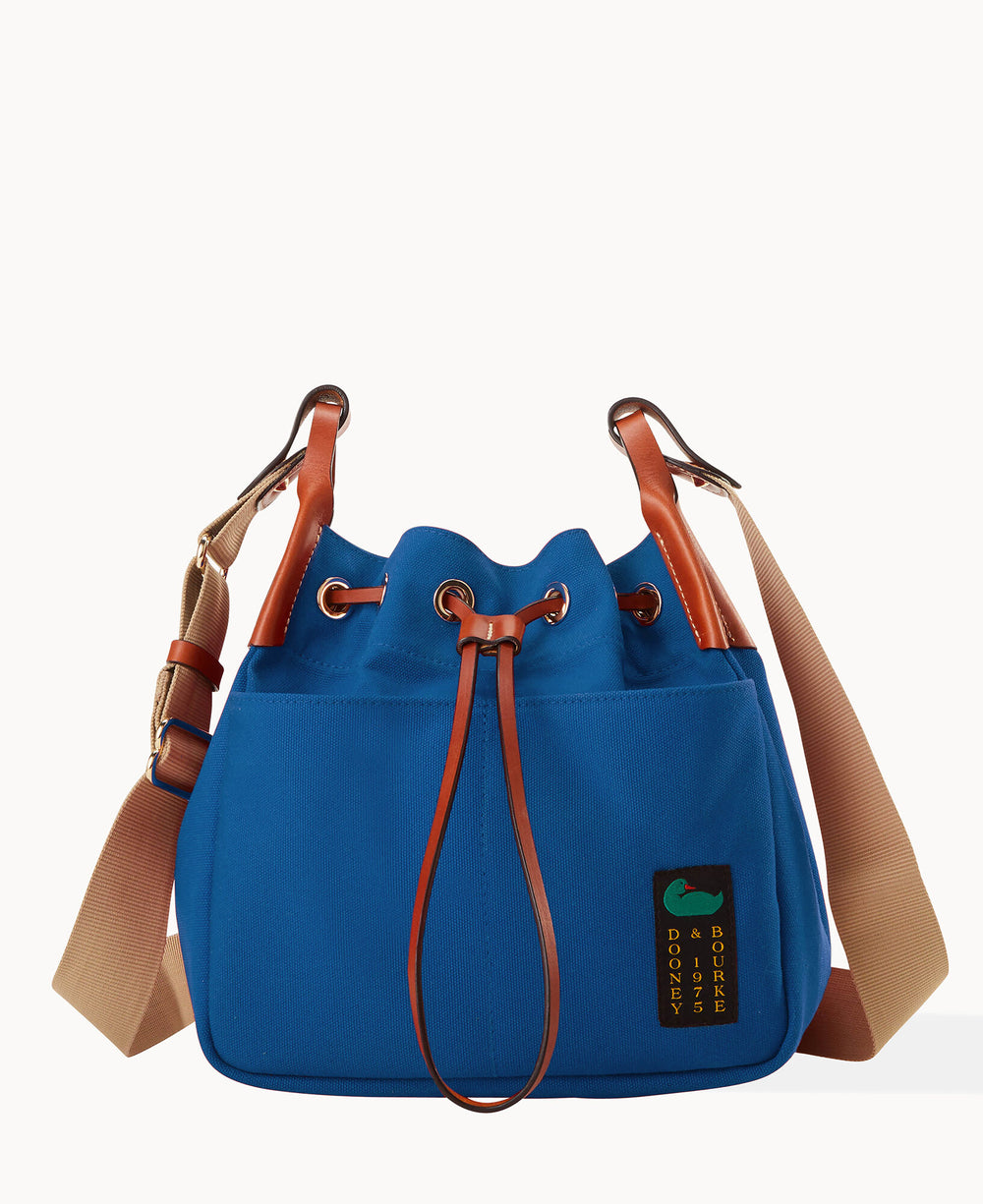A blue drawstring bucket bag with brown leather trim, tan adjustable shoulder strap, metal hardware, and a small rectangular Dooney & Bourke logo patch on the front.