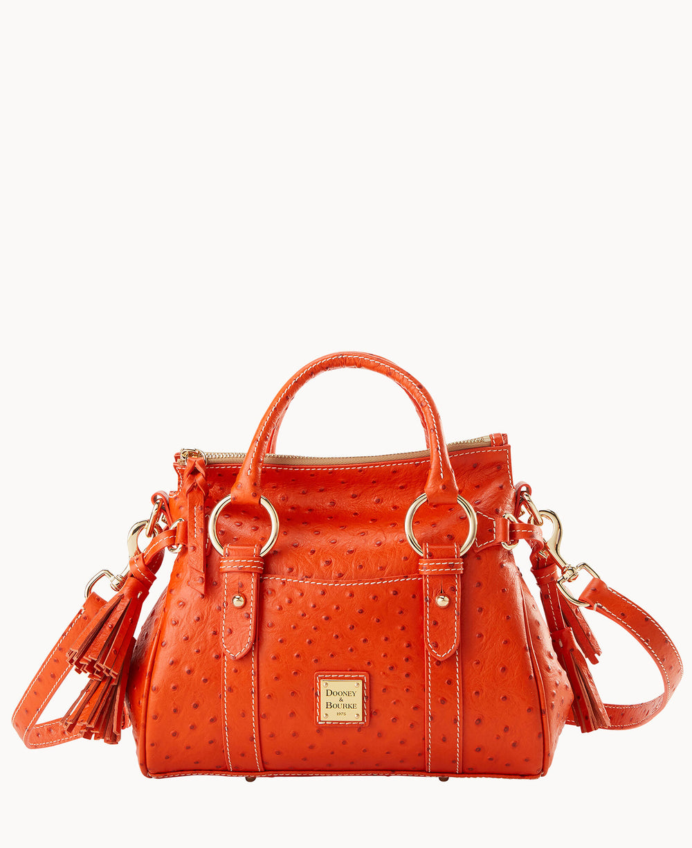 A bright orange textured leather handbag with gold hardware, two top handles, a detachable shoulder strap, tassel accents, and a Dooney & Bourke logo plate on the front.