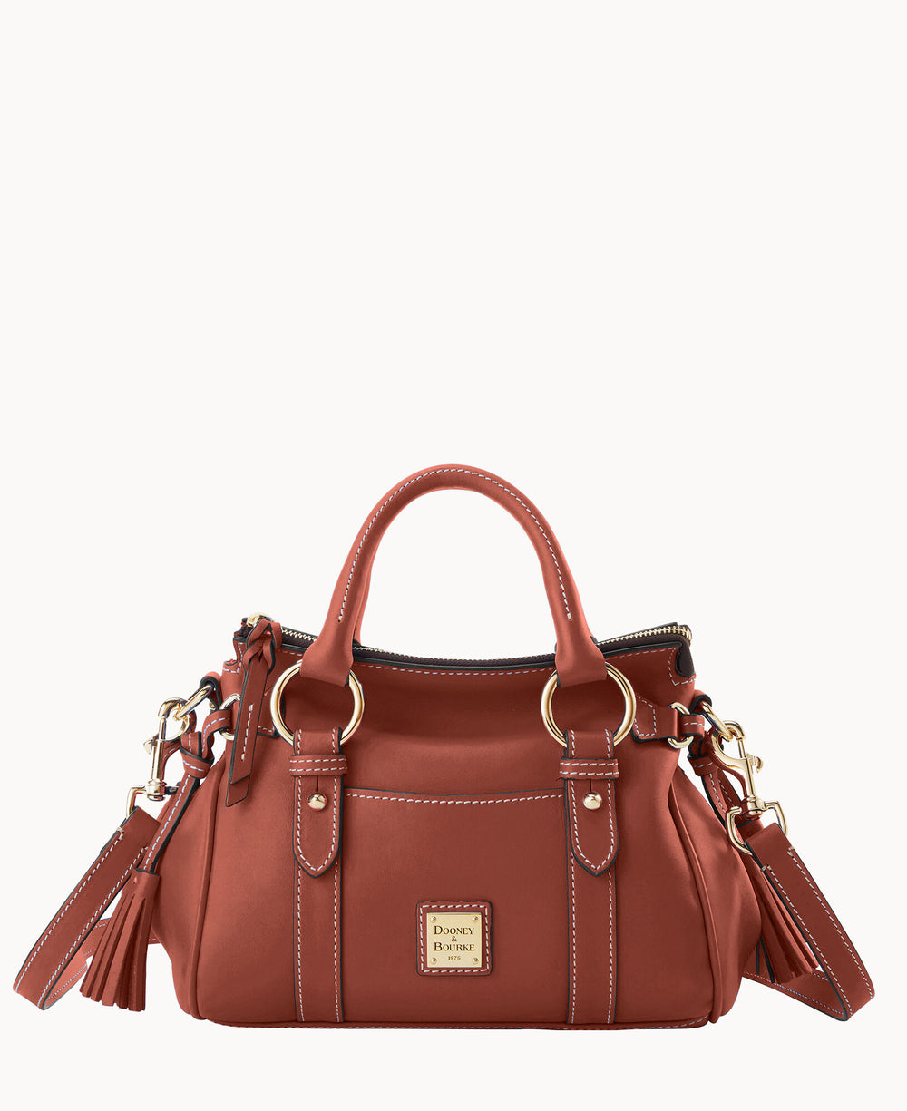 A medium-sized, brown leather handbag with two handles, gold hardware, white stitching, tassel accents, and a square Dooney & Bourke logo plaque on the front.