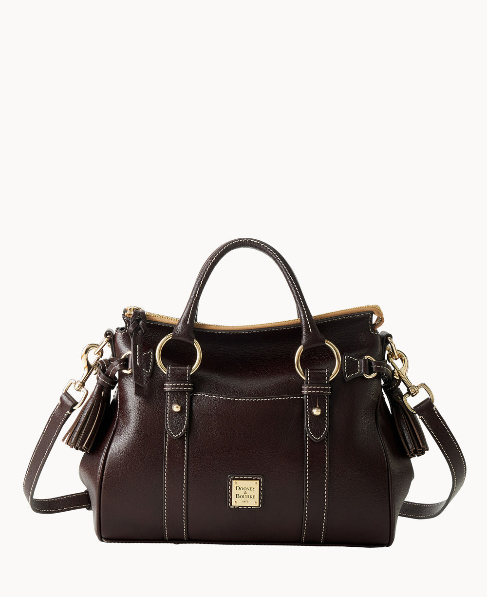 A dark brown leather handbag with gold hardware, double handles, a detachable shoulder strap, tassel accents, and a front logo plate, set against a white background.