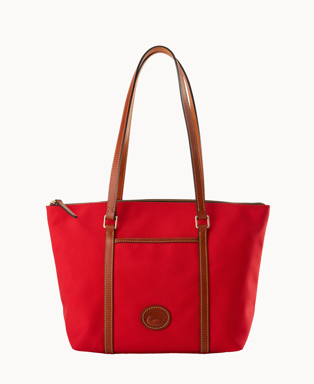 A red tote bag with brown leather handles and trim, featuring a small stitched logo patch on the front and a front slip pocket. The bag has a top zipper closure.