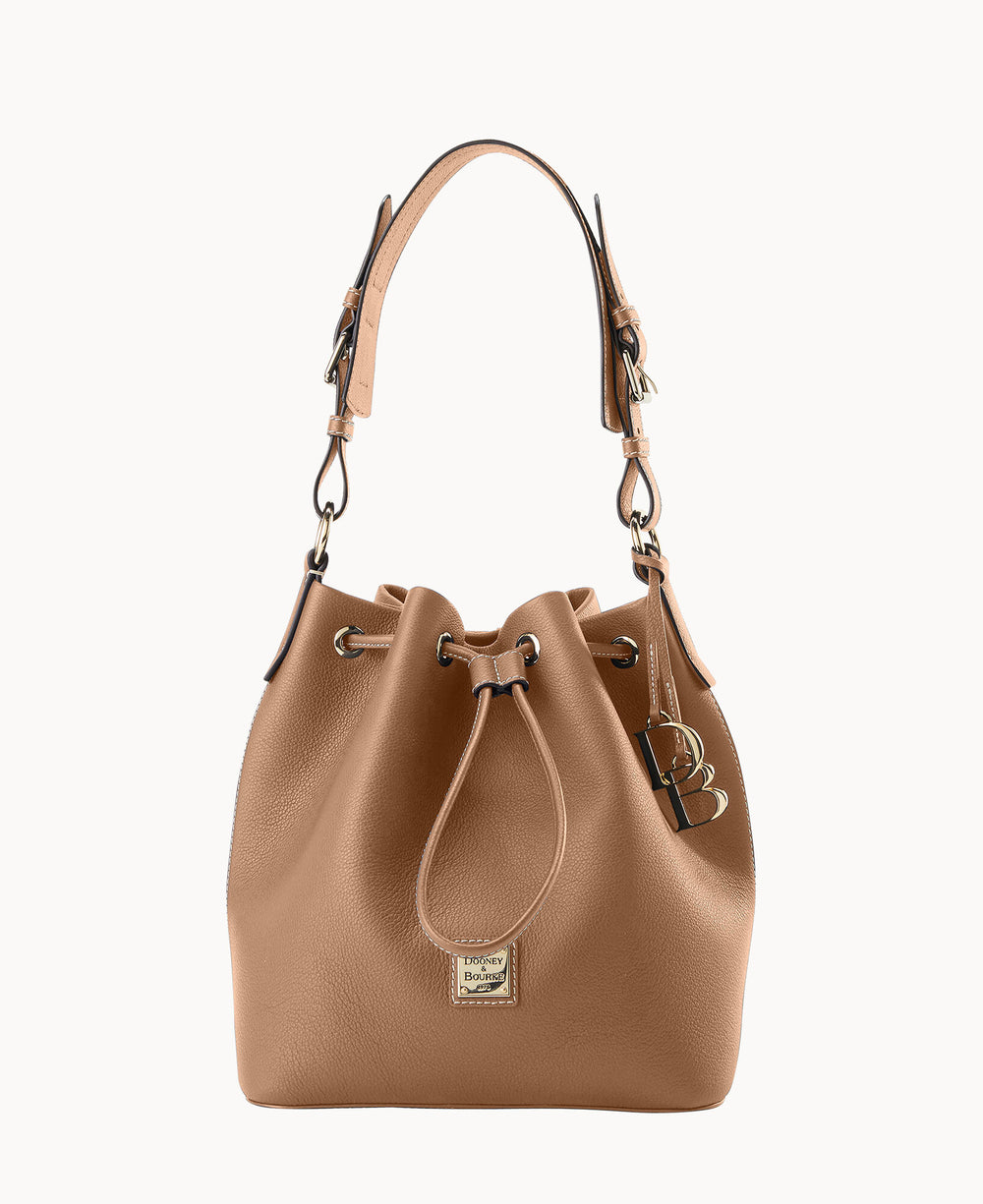 Tan leather bucket bag with a drawstring closure, adjustable shoulder strap, gold-tone hardware, and a small logo plaque on the front. A decorative keychain hangs from one of the side rings.