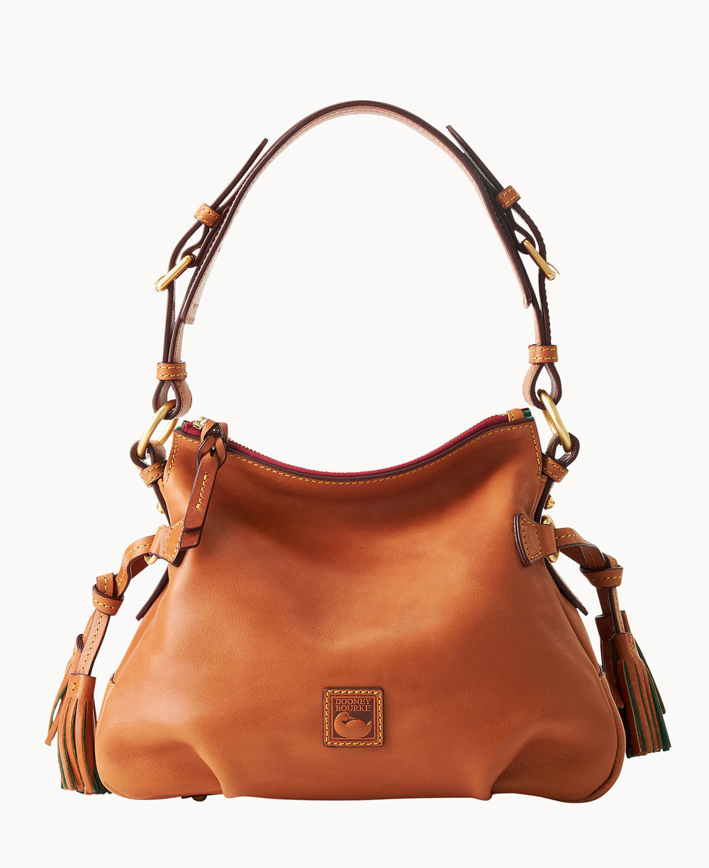 A medium-sized, tan leather handbag with a curved top, adjustable shoulder strap, gold hardware, side tassels, and a small logo patch on the front.