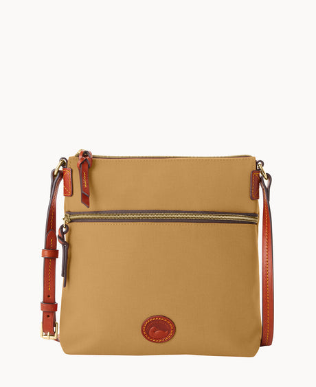 A tan crossbody bag with brown leather trim, a front zipper pocket, adjustable strap, and a small leather logo patch at the bottom center. The bag has gold-tone hardware and a zipper closure at the top.