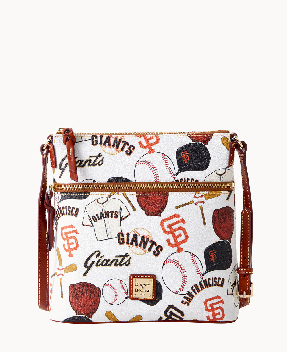 A white crossbody bag with brown leather trim features San Francisco Giants-themed prints, including baseballs, caps, gloves, jerseys, and team logos, along with front zippered pockets and gold hardware.
