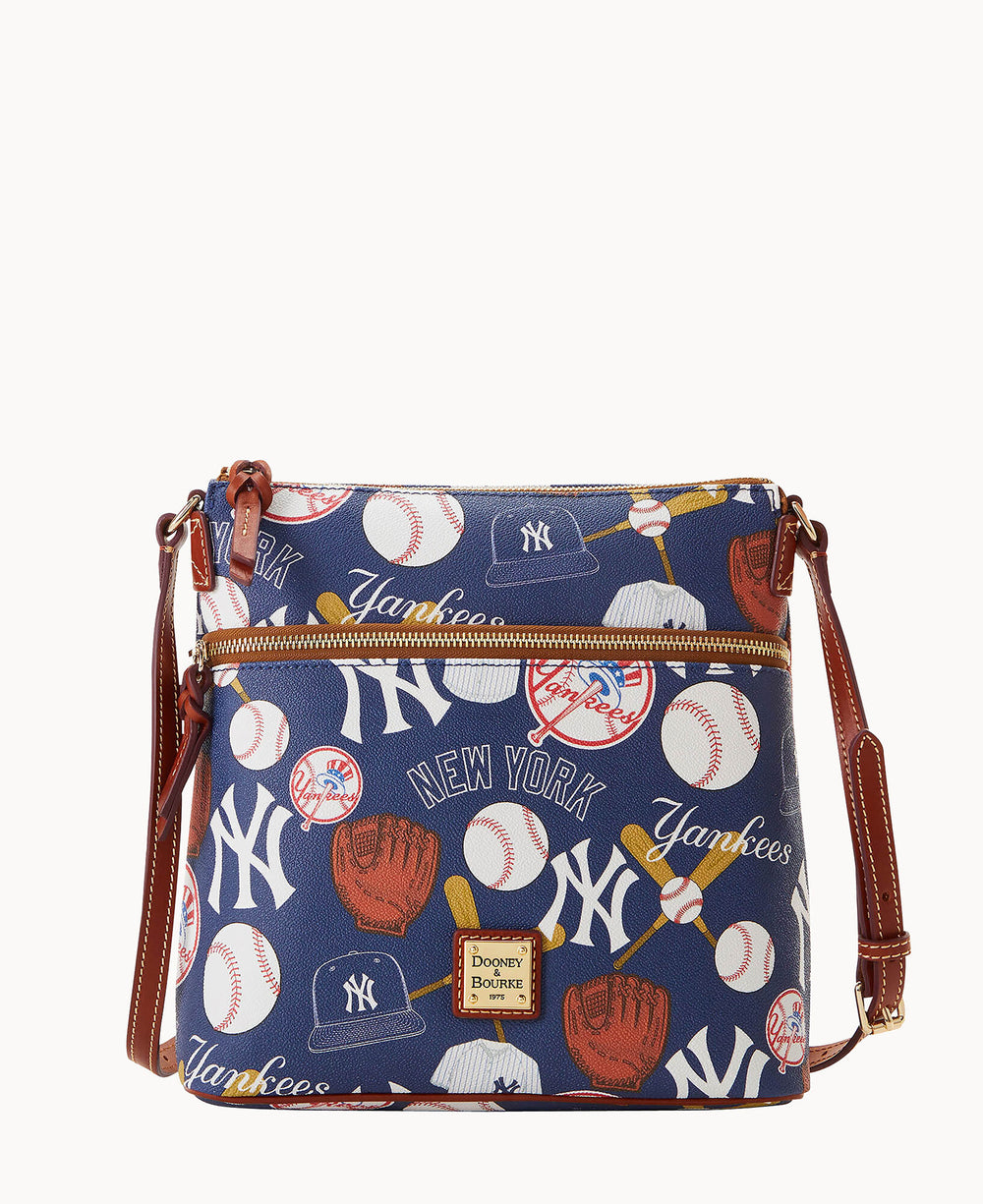 A navy crossbody bag with brown leather trim, decorated with New York Yankees logos, baseballs, gloves, caps, and Yankees and New York text in white and yellow.