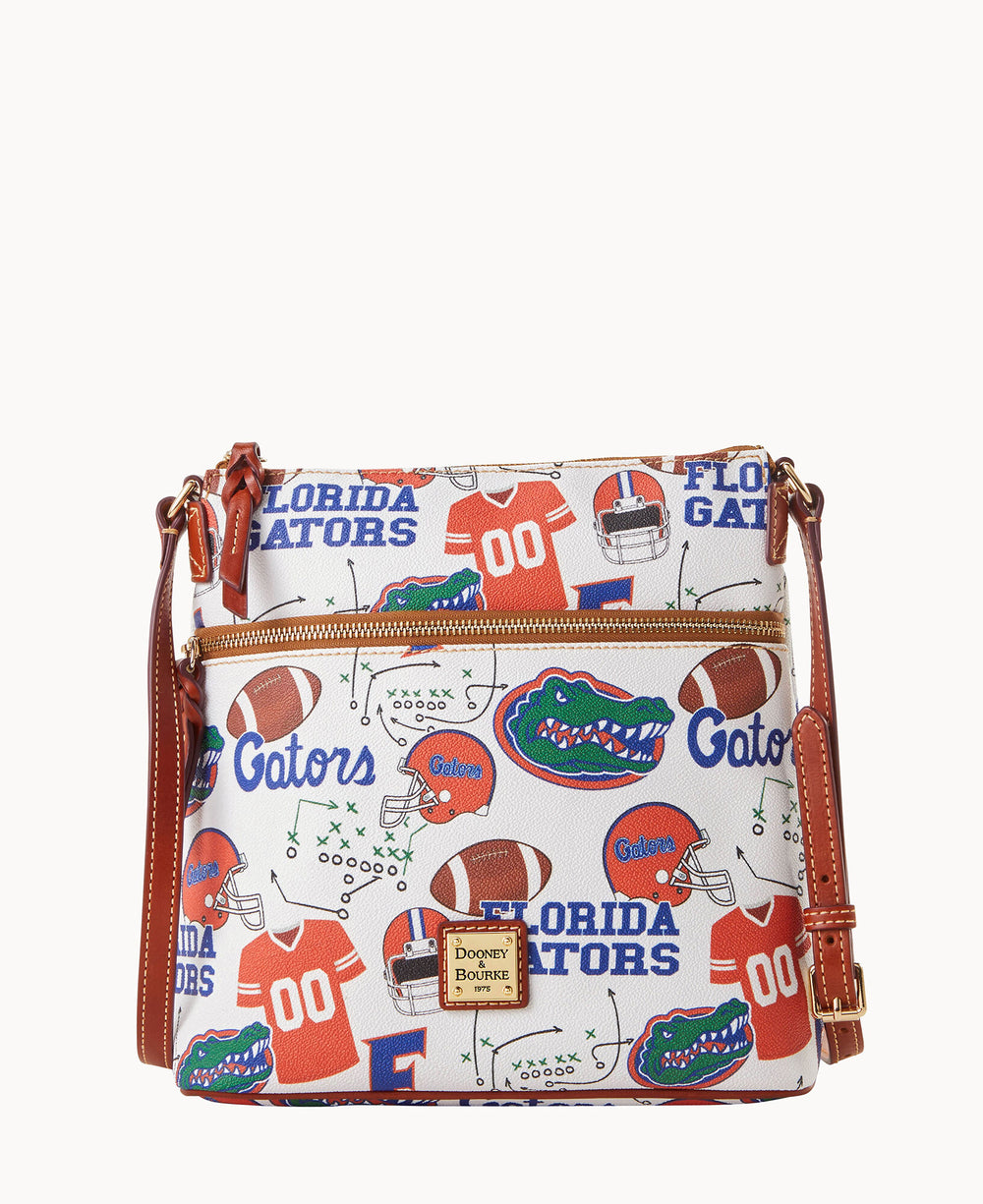 A white crossbody bag with brown leather straps, printed with Florida Gators logos, footballs, helmets, jerseys, and the words Florida Gators in blue and orange.