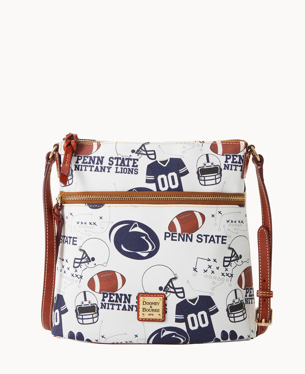 White crossbody bag with brown leather strap and trim, decorated with Penn State Nittany Lions logos, footballs, helmets, and jerseys. Front zipper pocket and Dooney & Bourke label at the bottom center.