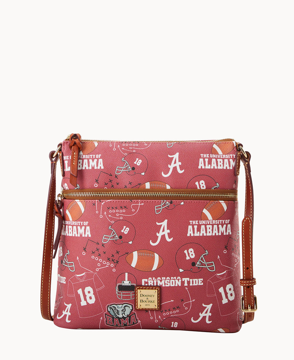 A red crossbody bag with brown leather accents, featuring University of Alabama-themed prints, including footballs, helmets, trophies, the letter A, and phrases like Crimson Tide and The University of Alabama.