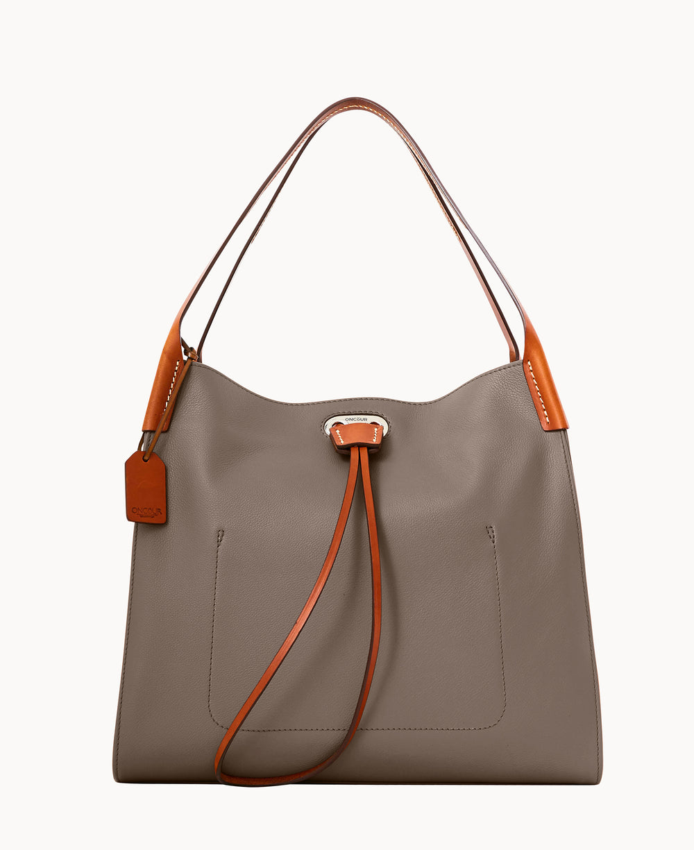 A taupe leather handbag with brown handles and a matching luggage tag. The bag has a simple design with a subtle front pocket and a long, thin strap tied at the front.