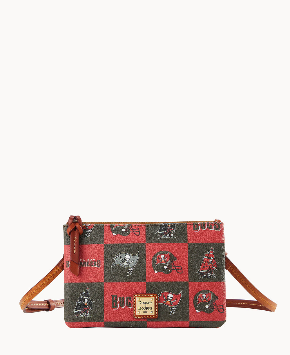 A small crossbody bag with a brown strap features red and dark squares patterned with Tampa Bay Buccaneers logos, including helmets, a pirate ship, and the word â€œBUCS.â€ The front displays a Dooney & Bourke logo patch.
