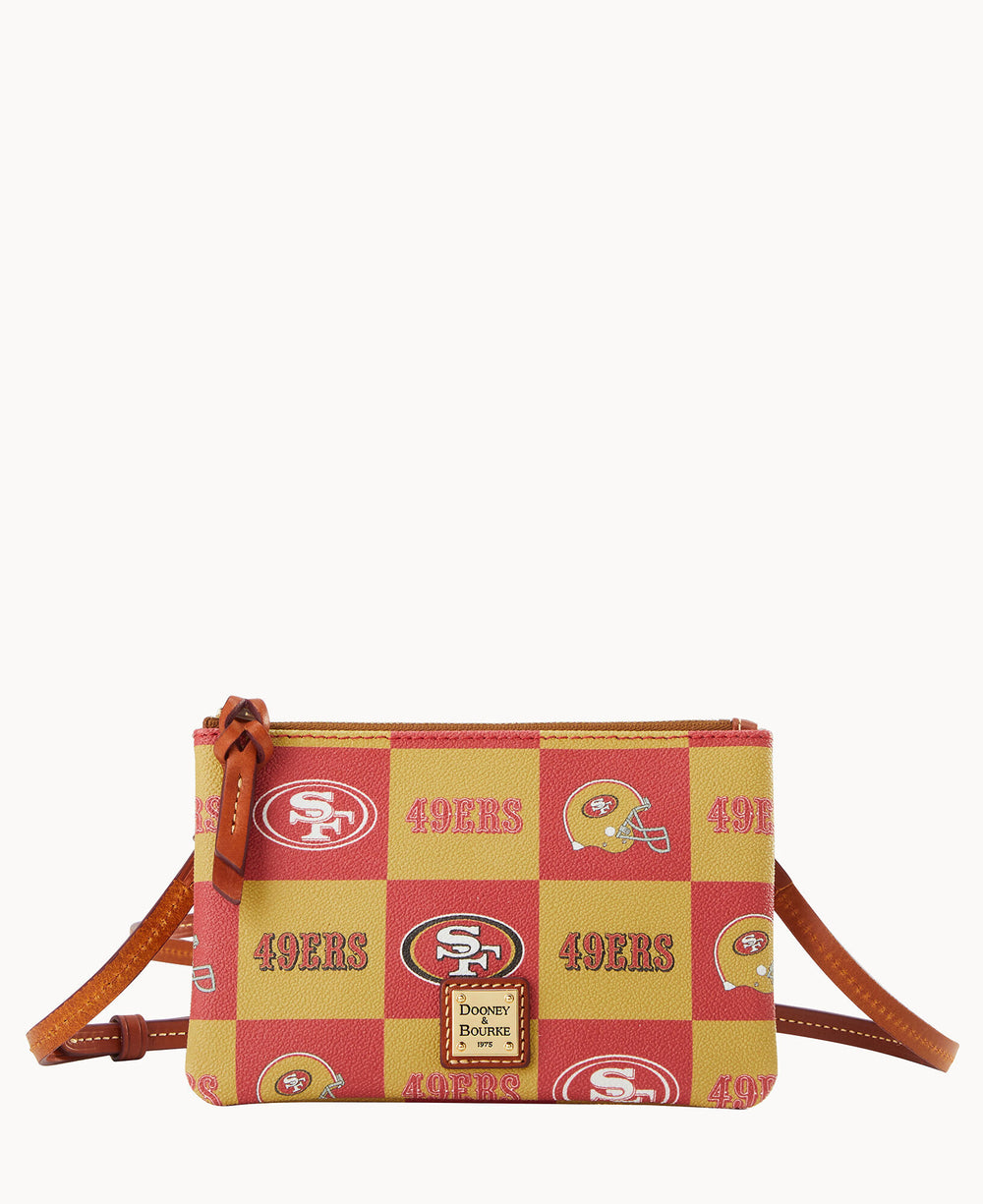 A small Dooney & Bourke crossbody bag features a red and gold checkered pattern with San Francisco 49ers logos, team name, and football helmets, plus tan leather trim and a logo patch on the front.