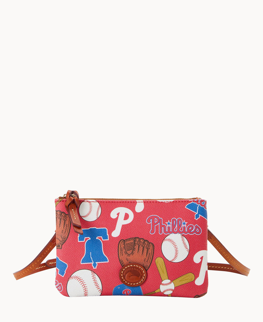 A small red crossbody bag featuring baseball-themed graphics, including gloves, bats, balls, jerseys, and the word Phillies with P logos, accented with brown leather details and a zipper closure.