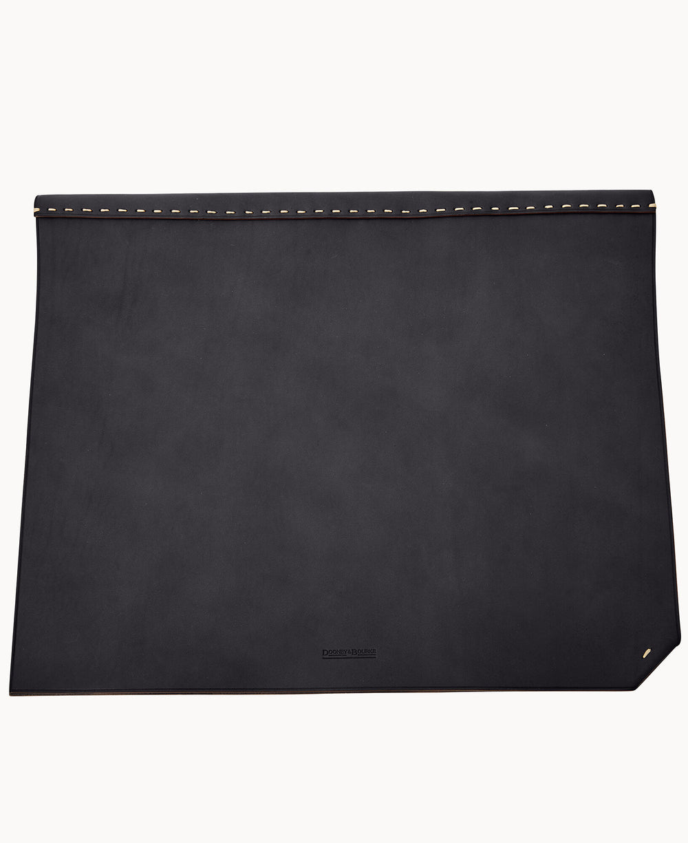 A large, rectangular black leather desk mat with a row of gold studs along the top edge and a small embossed logo near the bottom edge.