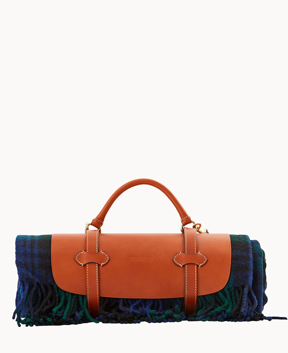 A rolled-up blue and green plaid blanket secured with brown leather straps and handles, resembling a stylish carrying case or bag, against a plain white background.