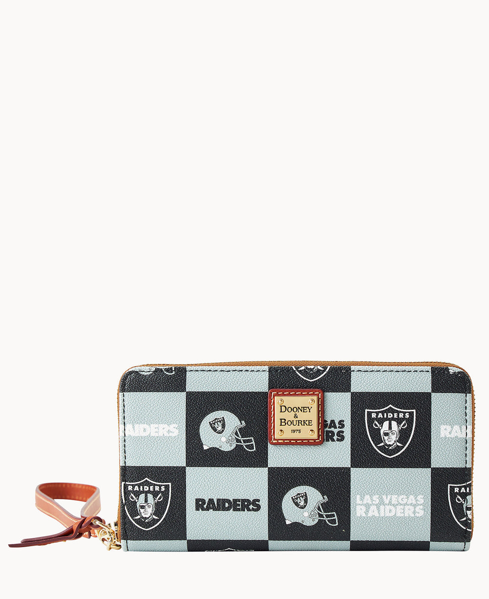 A zip-around wallet with a brown leather wrist strap, featuring a black and gray checkered pattern with Las Vegas Raiders logos, helmets, and the team name, plus a Dooney & Bourke label on the front.