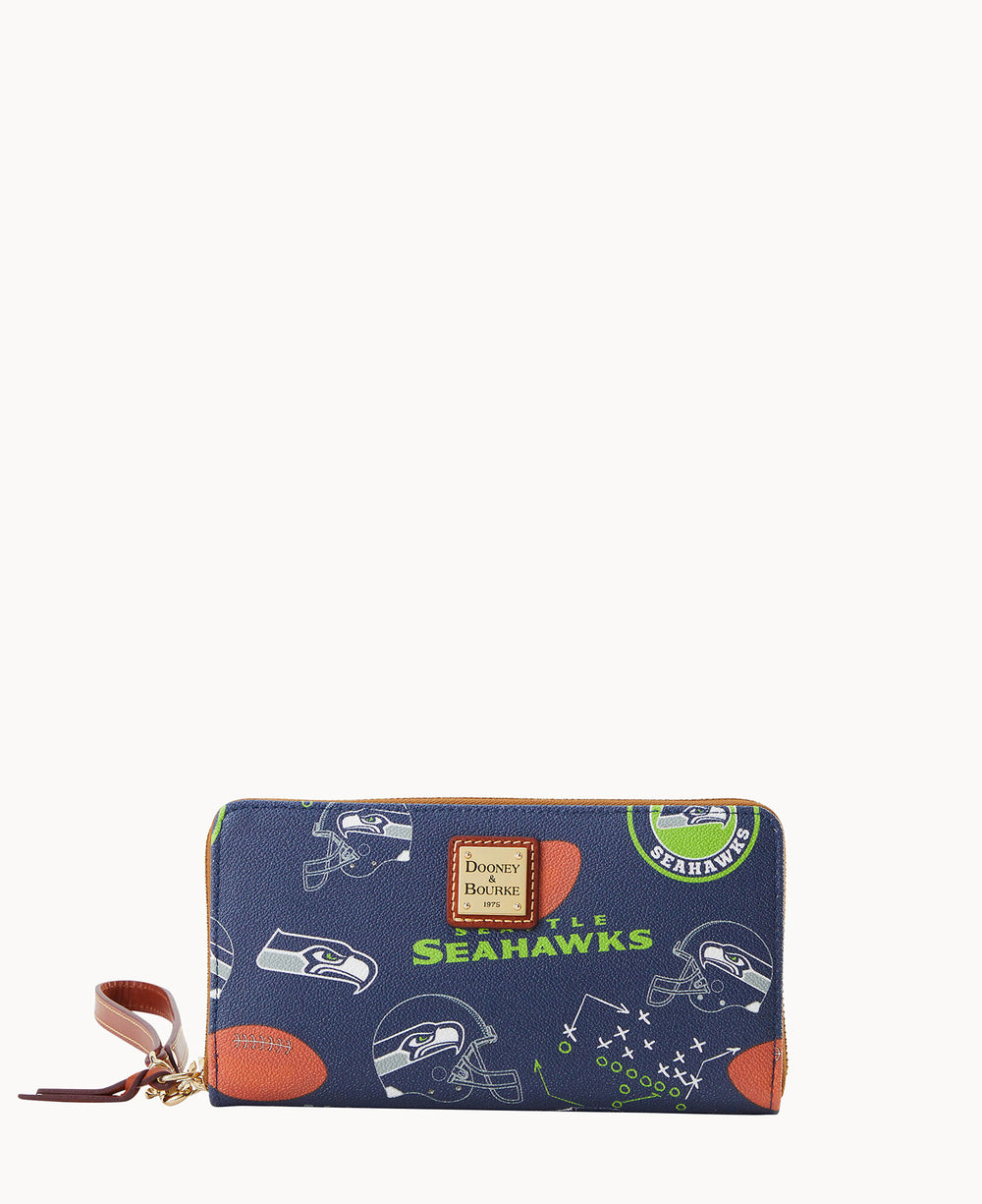 A navy blue zippered wallet featuring Seattle Seahawks logos, footballs, helmets, and play diagrams, with a brown leather wrist strap and a rectangular Dooney & Bourke label on the front.