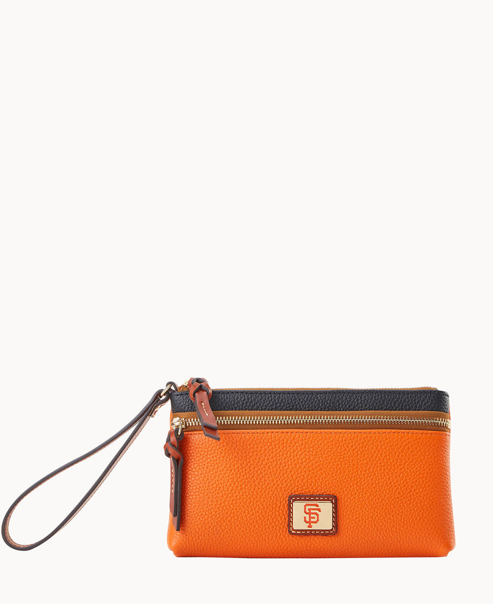 An orange leather wristlet pouch with a black top border, gold zipper, brown wrist strap, and a small square logo patch on the front.
