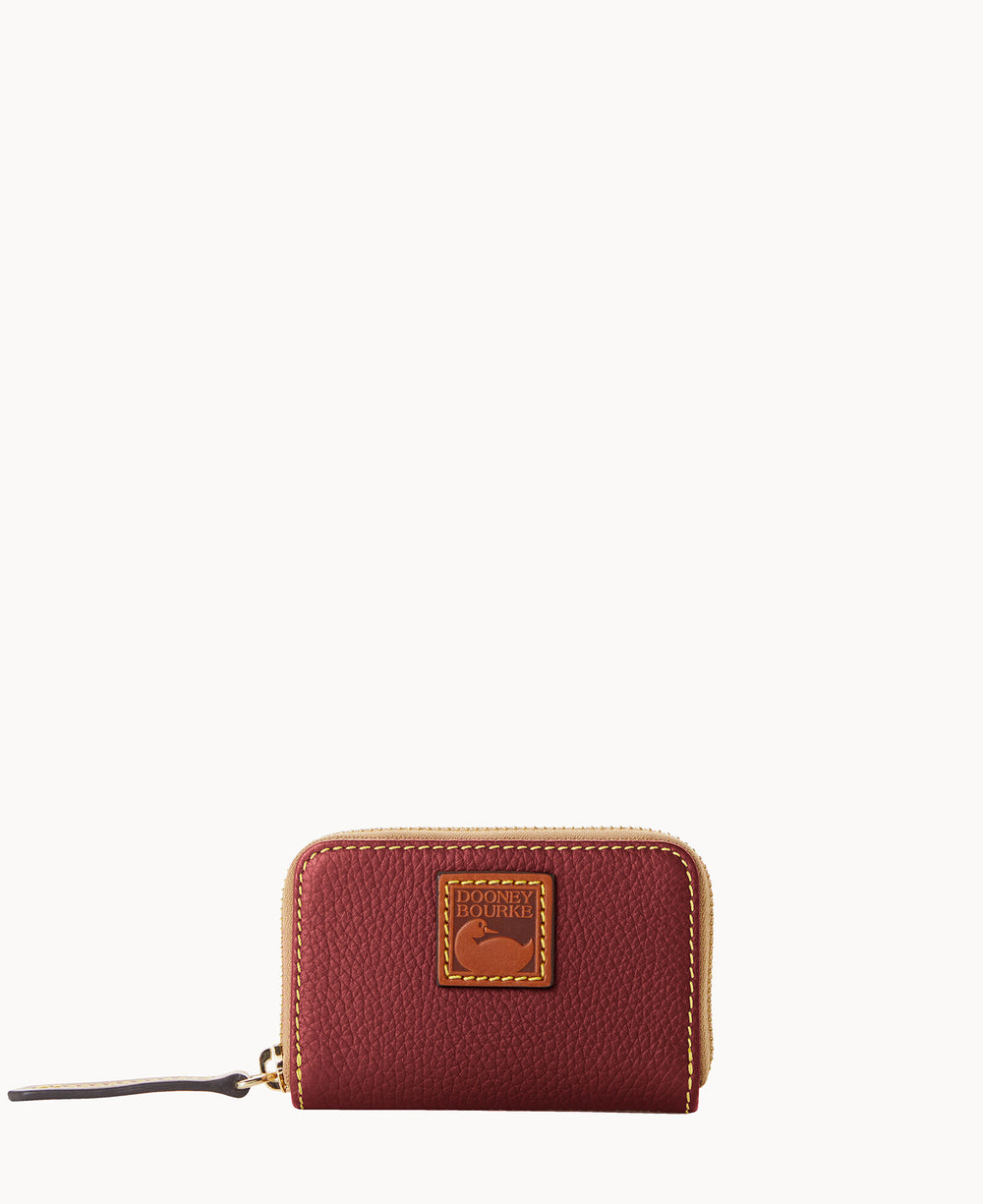 A small, burgundy leather zip wallet with a gold zipper and a tan leather logo patch on the front. The wallet has a textured finish and a zipper pull on the left side.
