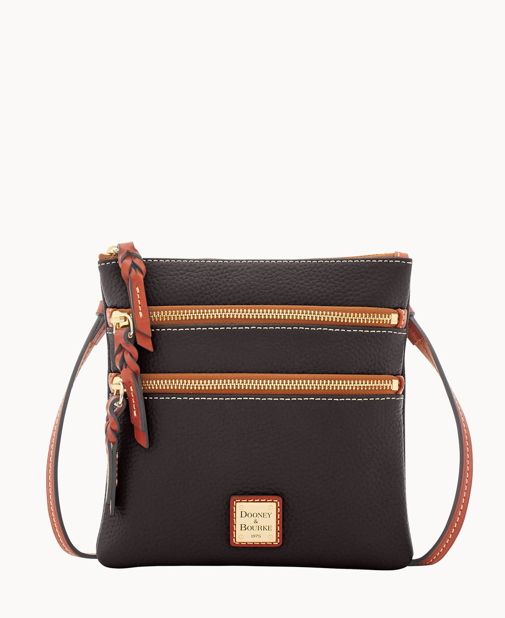 A small black leather crossbody bag with two front zippered pockets, gold hardware, brown leather accents, and a Dooney & Bourke logo patch on the front.