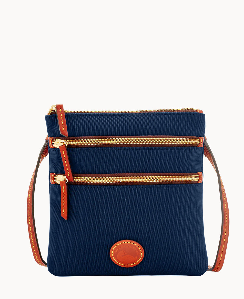 A navy blue crossbody bag with brown leather trim, three zippered compartments, a slim shoulder strap, and an oval leather logo patch on the front.