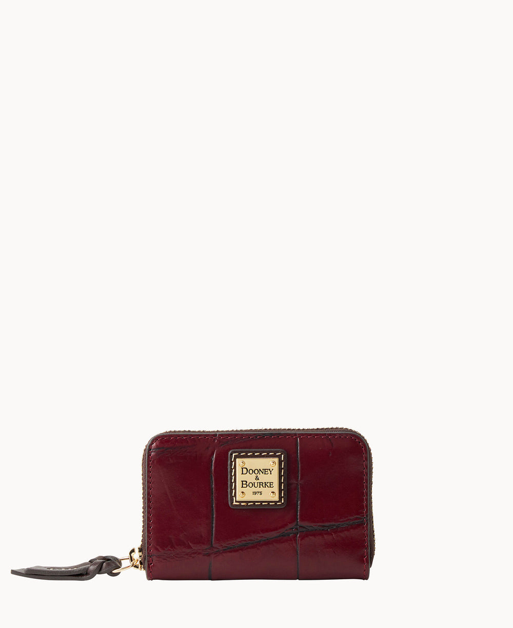 A small maroon Dooney & Bourke wallet with crocodile texture, gold logo plate on the front, zip closure, and a dark leather zipper pull, displayed against a white background.