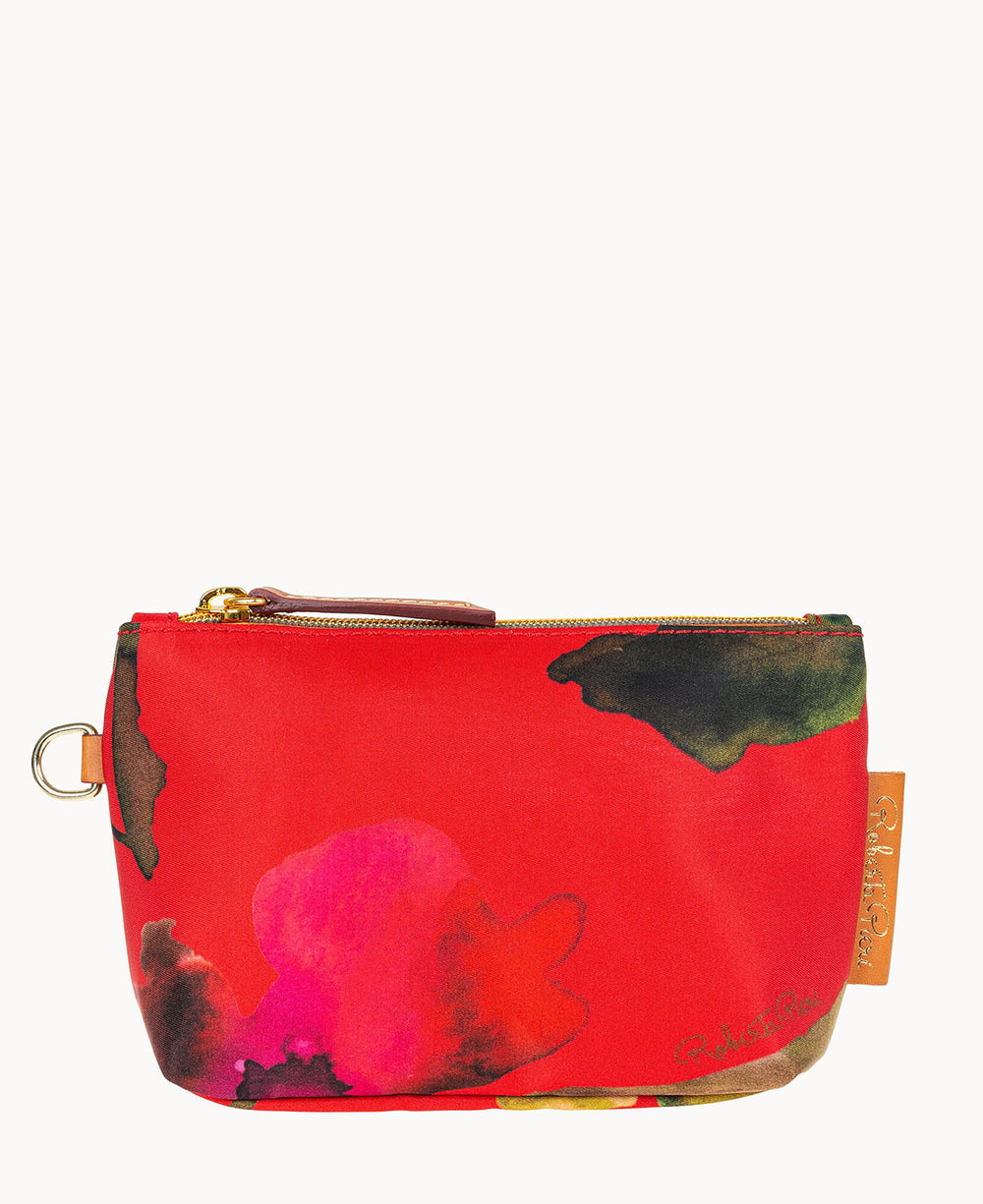A small zippered pouch with a vibrant red fabric featuring abstract splashes of pink, yellow, and black. The pouch has a gold zipper, a side tag, and a metal ring on one side.