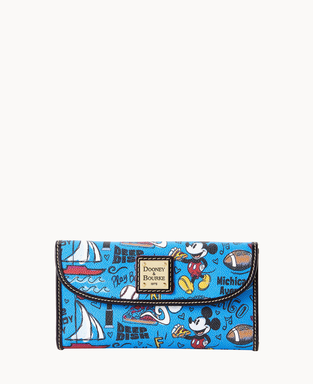 A blue Dooney & Bourke wallet featuring various images and doodles of Mickey Mouse, sailboats, footballs, and playful text, with a gold logo plaque on the front flap.